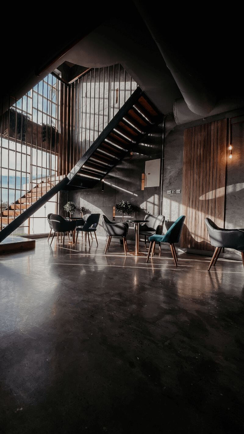 Industrial room with large windows, staircase, tables, chairs.